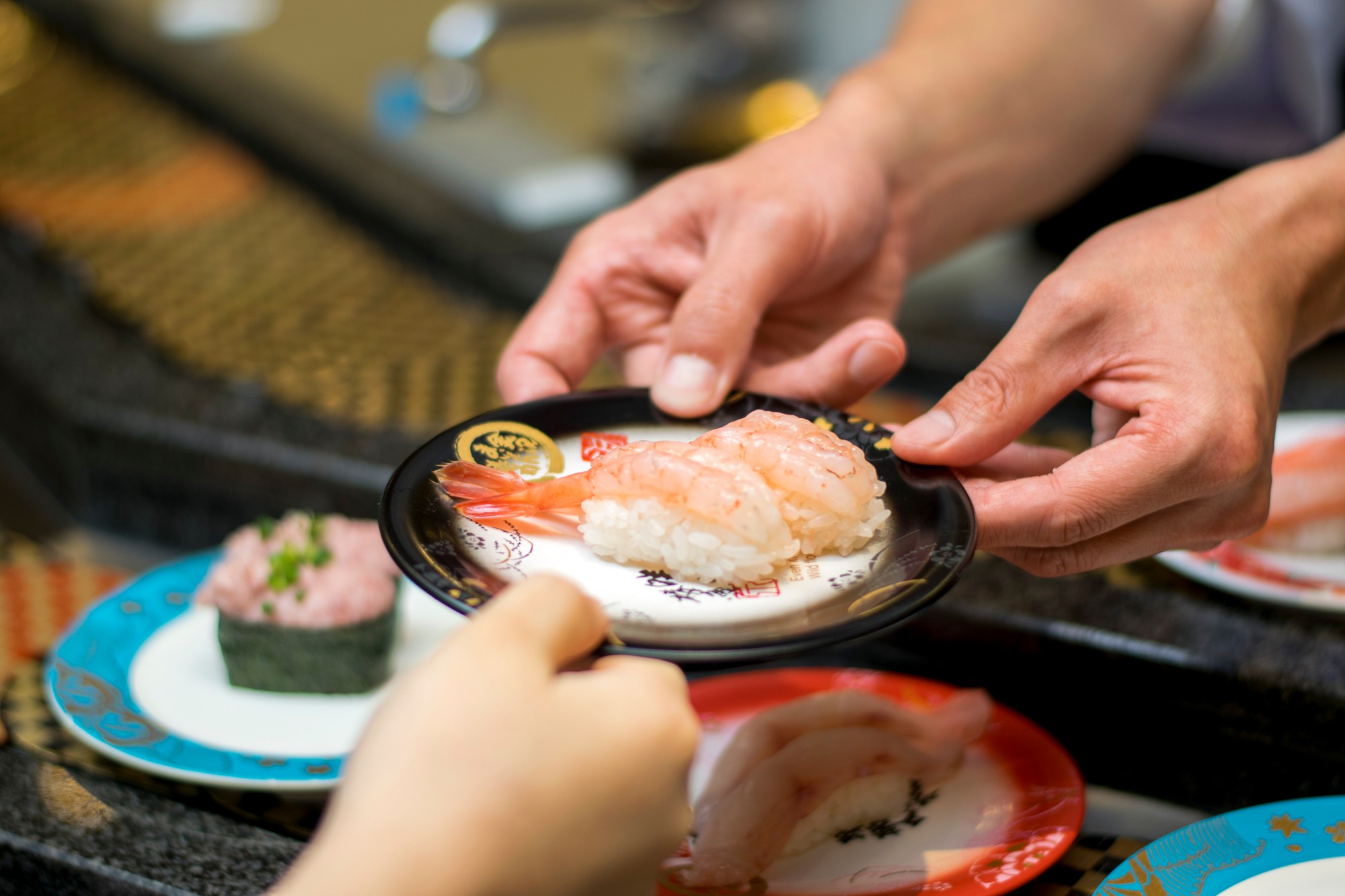 寿司の皿をお客様へお渡しする場面